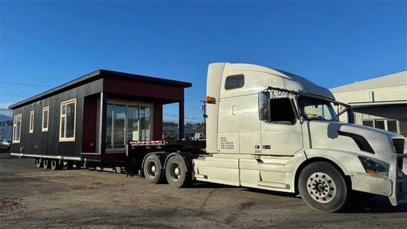A large, long hauling truck carrying a modular home in the back.